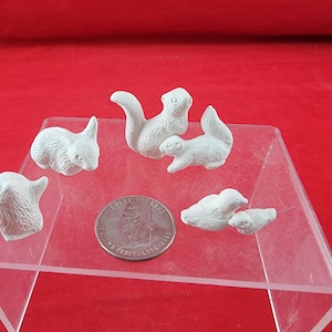 May include: A set of five small white unpainted ceramic animal figurines including a rabbit, two squirrels, and two birds, arranged around a silver United States quarter coin for scale, featuring detailed textures on each individual piece.