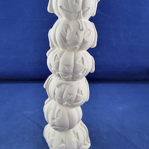 May include: A vertical stack of six unpainted white ceramic jack-o'-lanterns. Each pumpkin features carved triangular eyes, a triangular nose, and a wide, smiling mouth. The surface is matte and smooth, showing the raw bisque ceramic material.