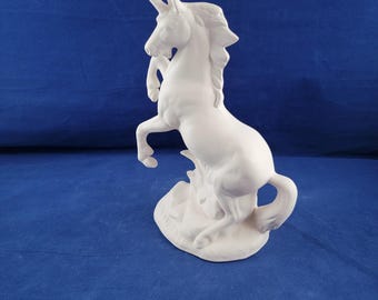 May include: White ceramic unicorn figurine standing on its hind legs with its head turned to the side. The unicorn has a flowing mane and tail.