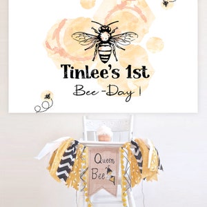 K&ouml;nnte beinhalten: Ein wei&szlig;er Hochstuhl mit einem gelben und schwarzen Banner, auf dem "Queen Bee" und eine Bienenillustration zu sehen sind. Das Banner ist mit gelben Bommeln verziert. Auf dem Tablett des Hochstuhls steht ein wei&szlig;er Cupcake. Im Hintergrund befindet sich eine Aquarell-Illustration einer Biene mit dem Text "Tinlee's 1st Bee-Day!"