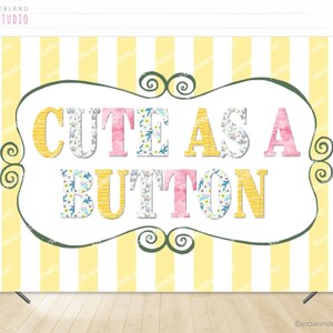 May include: A backdrop featuring a yellow and white striped design. The phrase "CUTE AS A BUTTON" is displayed within a decorative frame. The letters are yellow, pink, and decorated with floral patterns.
