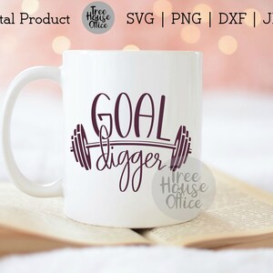 K&ouml;nnte beinhalten: Eine wei&szlig;e Keramiktasse mit einem violetten Design, auf dem "GOAL digger" steht, mit einer Langhantel und Gewichten auf beiden Seiten des Wortes "digger".