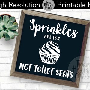 May include: A black chalkboard sign with white text that reads "Sprinkles are for cupcakes, not toilet seats". The sign is framed in wood and has a white cupcake graphic with the word "cupcakes" written on it.