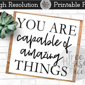 May include: White wooden sign with black text that reads "You are capable of amazing things".