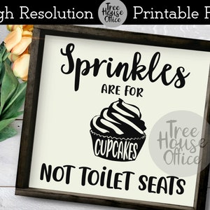 May include: A white sign with black text and a black cupcake graphic. The sign reads "Sprinkles are for cupcakes, not toilet seats".