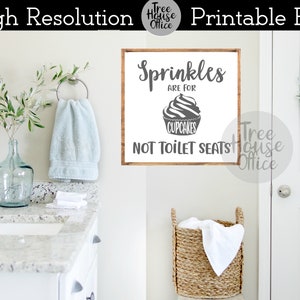 May include: A white sign with a wooden frame and black text that reads "Sprinkles are for cupcakes, not toilet seats". The sign is hanging on a white wall in a bathroom.