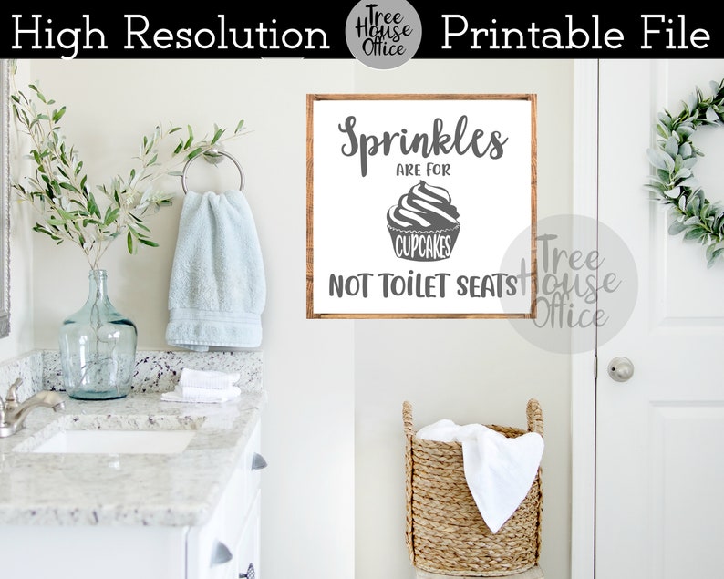 May include: A white sign with a wooden frame and black text that reads "Sprinkles are for cupcakes, not toilet seats". The sign is hanging on a white wall in a bathroom.