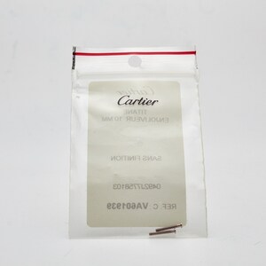 May include: A small clear plastic bag with a red zipper seal. The bag contains two small silver metal pins. The bag has a white label with the text 'Cartier', 'ENVOLUTION 10 MM', 'SANS FINITION', '04297728103', 'REF: C.VAG01829'. 