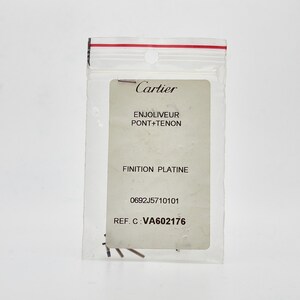 May include: A white card with black text in a clear plastic bag. The text reads: 'Cartier', 'Enjoliveur Pont + Tenon', 'Finition Platine', '0692J5710101', 'REF. C: VA602176'