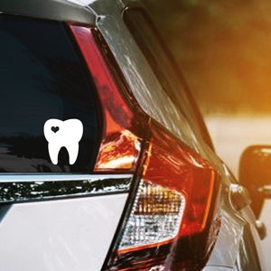 May include: A white car with a white tooth sticker on the back window. The tooth has a small heart in the center.