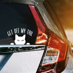 May include: A white car with a cat sticker on the back window. The sticker says "Get off my tail".