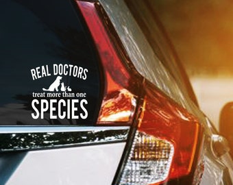 May include: A white vinyl sticker on the back of a silver car. The sticker says "Real Doctors treat more than one SPECIES".
