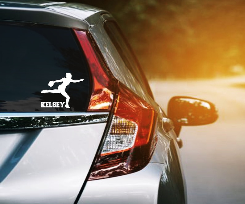 May include: White vinyl car decal featuring a silhouette of a discus thrower in action. The name "KELSEY" is printed in bold, capital letters below the athlete. The decal is affixed to the rear window of a silver car.