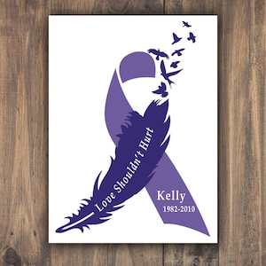 Puede incluir: Cinta morada con un dise&ntilde;o de pluma y el texto "El amor no deber&iacute;a doler" y el nombre "Kelly" con las fechas 1982-2010.