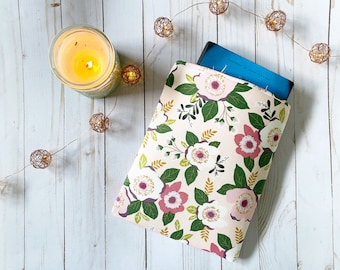 May include: A pink floral book sleeve with a book inside. The book sleeve has a white background with pink and white flowers and green leaves. The book is blue and has text on the cover.