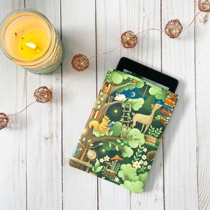 Peut inclure: Une housse pour liseuse électronique avec un motif de forêt comprenant un écureuil, un cerf et un lapin. La housse est de couleur verte, marron et blanche avec un design fantaisiste comprenant une maison dans les arbres, une échelle et une lune.