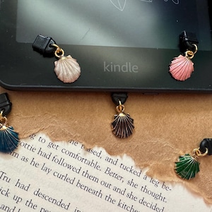 May include: Four different colored seashell charms on black clips. The charms are attached to a black e-reader with the word "kindle" printed on it.