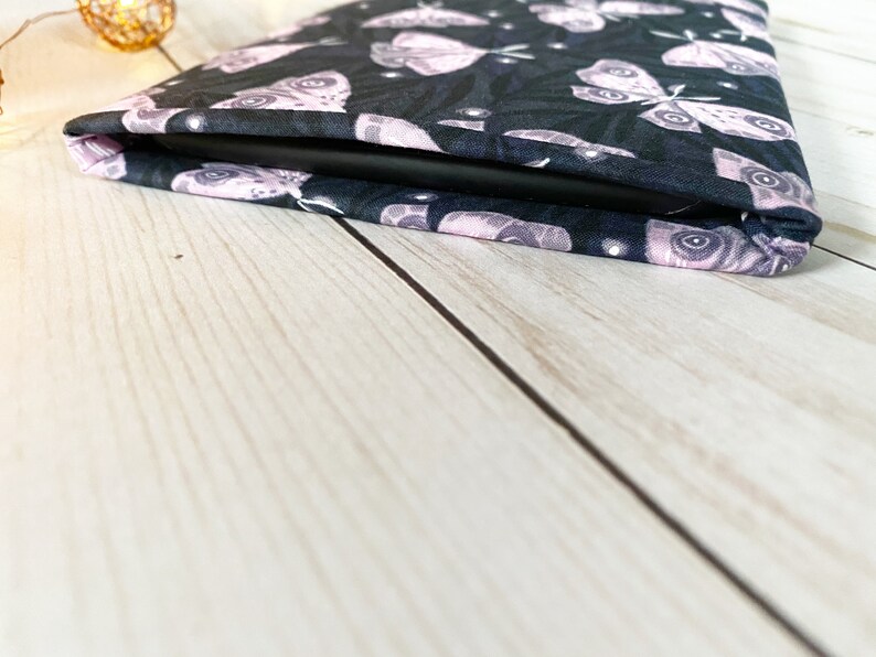 K&ouml;nnte beinhalten: Eine schwarze und rosafarbene Tableth&uuml;lle aus Stoff mit einem Muster aus Motten. Die H&uuml;lle ist zusammengefaltet und das Tablet ist nicht sichtbar.