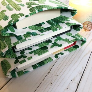May include: A stack of books covered in a white fabric book cover with a green cactus print.