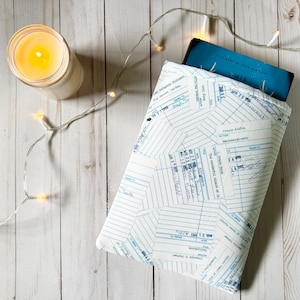 Könnte beinhalten: Eine weiße Buchhülle mit einem blau-weißen Muster. Die Hülle ist aus Stoff und hat einen Reißverschluss. Die Hülle ist mit einem Muster aus blauen Linien und Zahlen verziert, das an ein Notizbuch erinnert.