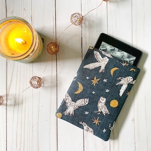 Op de afbeelding: Een donkerblauwe e-reader hoes met een wit uil en maan patroon. De hoes heeft een gouden ster en halve maan ontwerp. De e-reader zit in de hoes.