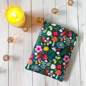 May include: A green fabric pouch with a colorful floral and mushroom print. The pouch is lying on a white wooden surface.