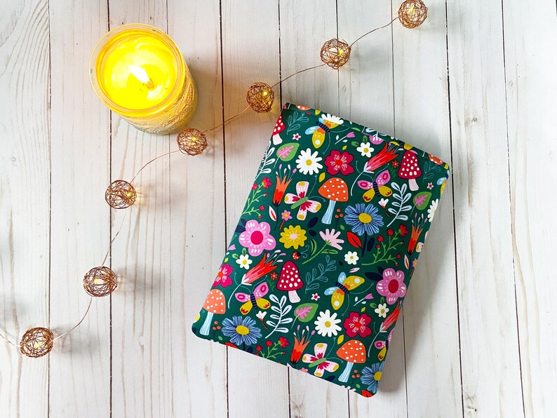 May include: A green fabric pouch with a colorful floral and mushroom print. The pouch is lying on a white wooden surface.