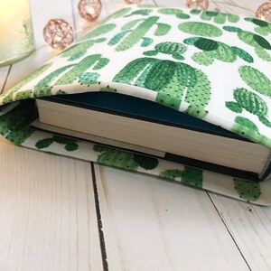 May include: A white book cover with a green cactus pattern. The cover is folded over a book with a teal blue spine.
