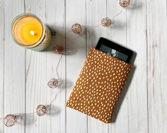 May include: A brown and white patterned e-reader cover with white polka dots. The e-reader is inside the cover and the screen is visible.