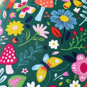 May include: A green fabric with a repeating pattern of colorful flowers, butterflies, and mushrooms. The flowers are in shades of pink, yellow, blue, and white. The butterflies are yellow, pink, and blue. The mushrooms are red with white spots.