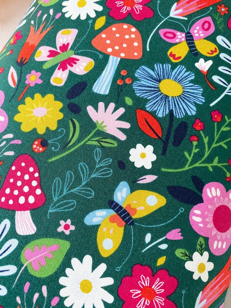 May include: A green fabric with a repeating pattern of colorful flowers, butterflies, and mushrooms. The flowers are in shades of pink, yellow, blue, and white. The butterflies are yellow, pink, and blue. The mushrooms are red with white spots.