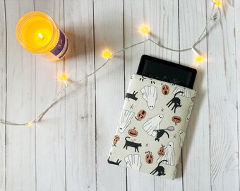 Pode incluir: Uma capa para leitor de e-books com padrão branco e preto com fantasmas, abóboras e gatos pretos. A capa é projetada para um leitor de e-books Kindle.