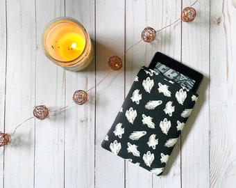 May include: A black e-reader with a white ghost pattern cover. The e-reader is on a white wooden surface with a string of copper lights and a candle.