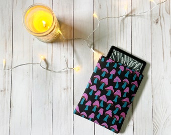 Puede incluir: Una funda negra para lector electrónico con un patrón de setas en rosa y azul. La funda está sobre una superficie de madera blanca con una cadena de luces.