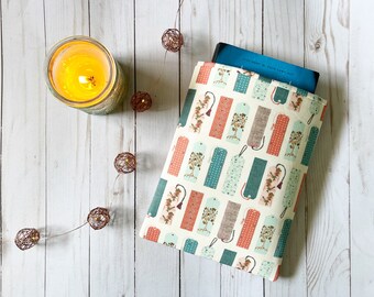 Puede incluir: Una funda para libro con fondo crema y un patrón repetido de marcapáginas coloridos. Los marcapáginas tienen una variedad de diseños, que incluyen árboles, flores y formas geométricas.