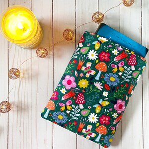 May include: A green book sleeve with a colorful floral pattern featuring butterflies, mushrooms, and flowers. The sleeve is made of fabric and has a zipper closure.