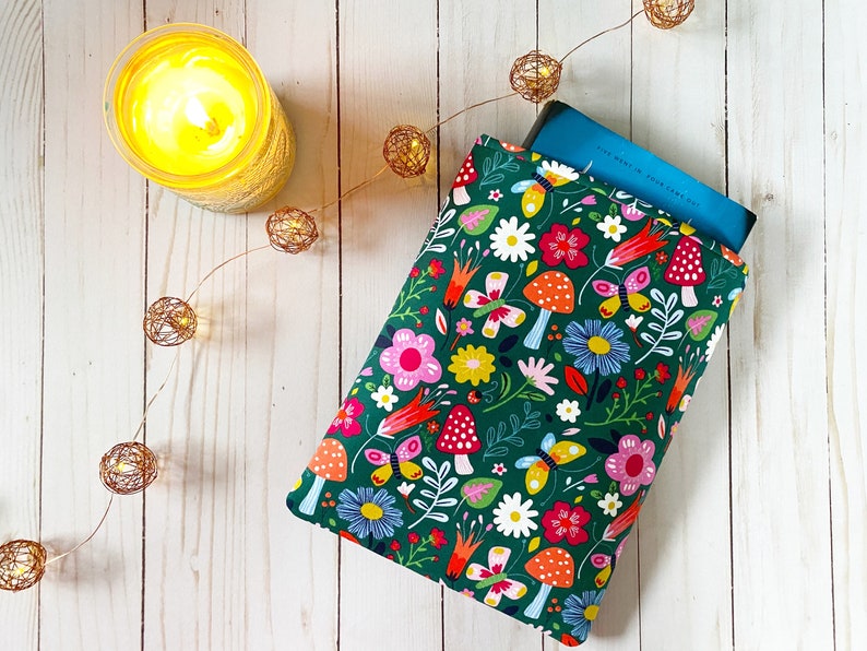 May include: A green book sleeve with a colorful floral pattern featuring butterflies, mushrooms, and flowers. The sleeve is made of fabric and has a zipper closure.