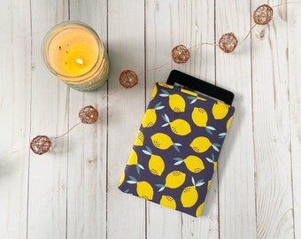 May include: A purple and yellow e-reader case with a lemon print. The case is on a white wooden surface with a string of lights.