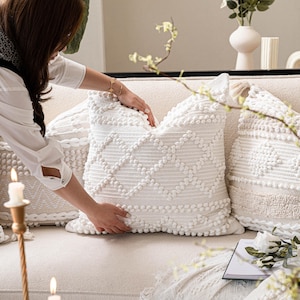 May include: White throw pillows with a textured, tufted design. The pillows are arranged on a white couch with a white blanket.