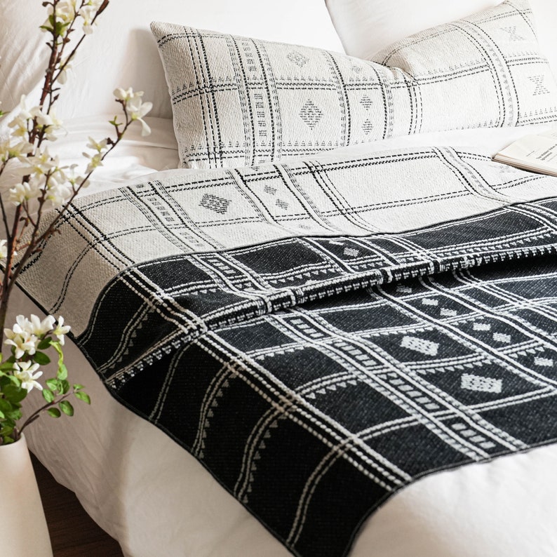 Puede incluir: Manta de tiro de patr&oacute;n blanco y negro con un dise&ntilde;o geom&eacute;trico. La manta est&aacute; doblada en una cama blanca con dos almohadas blancas con fundas de almohada de patr&oacute;n blanco y negro.