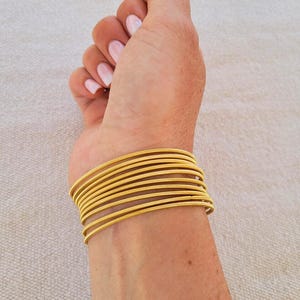 May include: A stack of gold-colored bangle bracelets on a person's wrist.