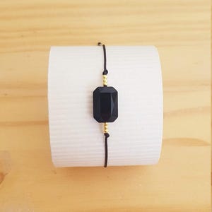 Peut inclure: Un bracelet avec une pierre noire et des perles dorées sur un cordon noir.