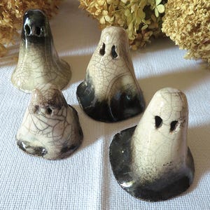 Peut inclure: Quatre figurines de fantômes en céramique avec une finition émaillée craquelée. Chaque pièce présente un corps de couleur crème avec des nuances noires fumées à la base et deux petites ouvertures oculaires creuses. Les tailles varient.