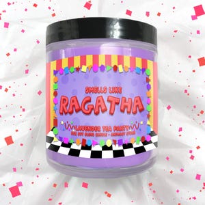 Puede incluir: Una vela de color lavanda en un tarro transparente con tapa negra. La etiqueta dice "Smells Like Ragatha Lavender Tea Party". La etiqueta tiene un fondo morado con formas coloridas y un patr&oacute;n de cuadros blanco y negro en la parte inferior.
