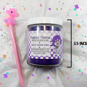 May include: Purple soy candle with a white label featuring an illustration of Kokichi Ouma from Danganronpa V3. The label reads "Kokichi Ouma Ultimate Supreme Leader, SCENT: GRAPE SODA, DANGANRONPA V3, 8oz Hand Poured Soy Blend Candle, ANIMACY STORE". The candle is 8.9 cm tall.