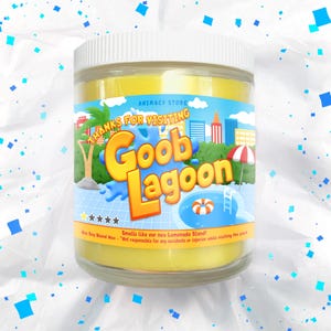 May include: A clear glass jar filled with yellow wax, labeled "Goob Lagoon." The label features a cartoon scene with a pool, palm trees, and the text "Thanks for Visiting." The jar has a white lid and is surrounded by blue and white confetti.