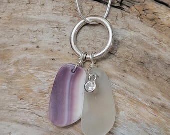 May include: A silver chain necklace with a circle pendant and two charms. One charm is a purple and white seashell, the other is a clear glass piece. A small clear rhinestone dangles from the glass charm.