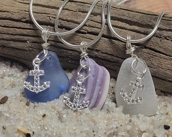 May include: Three silver chain necklaces with sea glass pendants and silver anchor charms. The sea glass is blue, purple and white.
