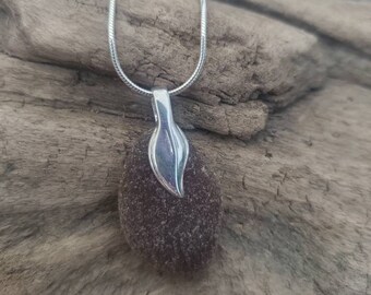 May include: A silver chain necklace with a brown sea glass pendant and a silver leaf charm.