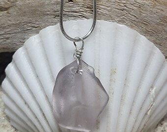 May include: A silver chain necklace with a light purple sea glass pendant. The pendant is wrapped in silver wire and hangs from a silver chain.